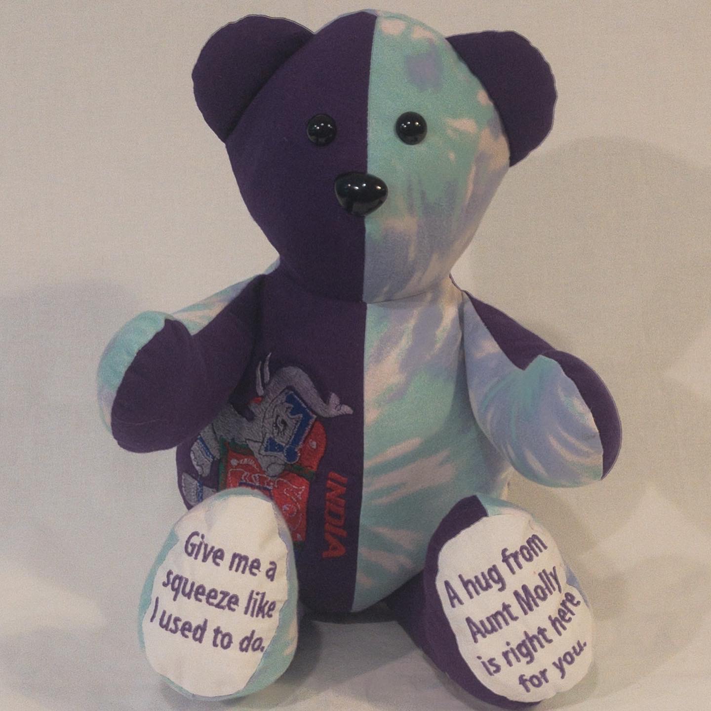 Purple and tie-dye memory bear from Aunt Molly's shirts with 'Give me a squeeze' embroidered on the feet
